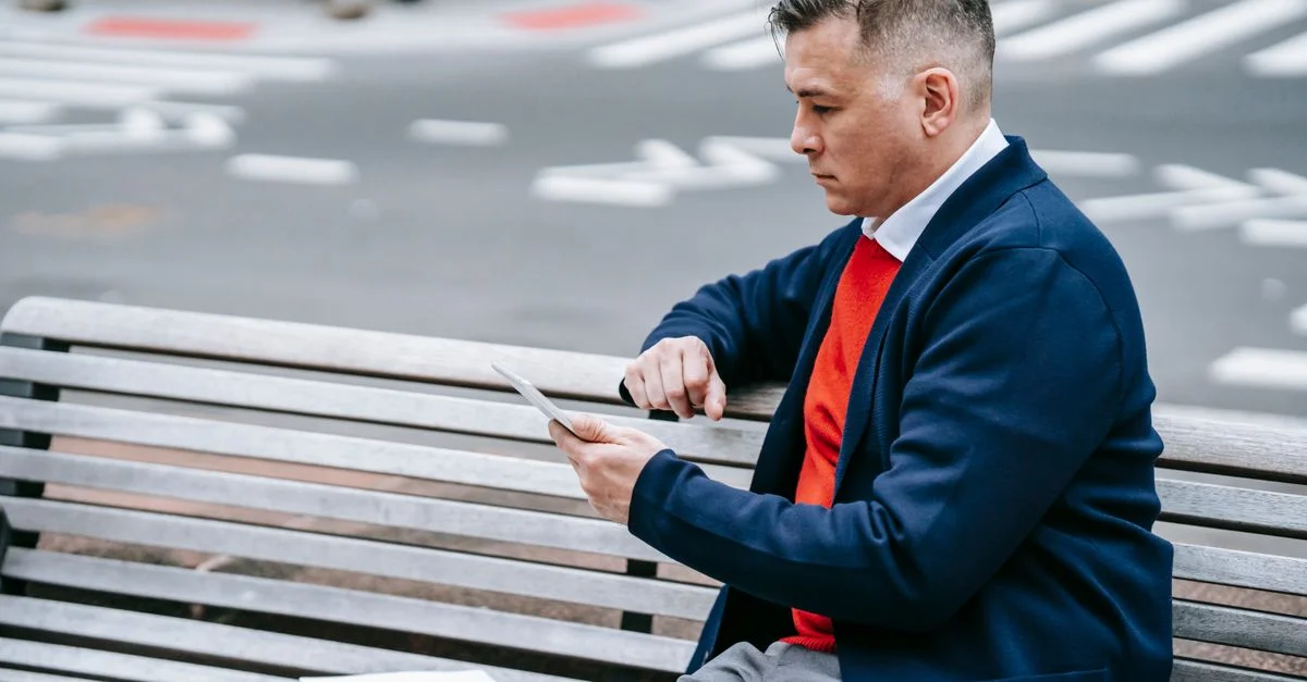 Homme professionnel utilisant une tablette sur un banc de ville tout en profitant d'un environnement urbain extérieur.