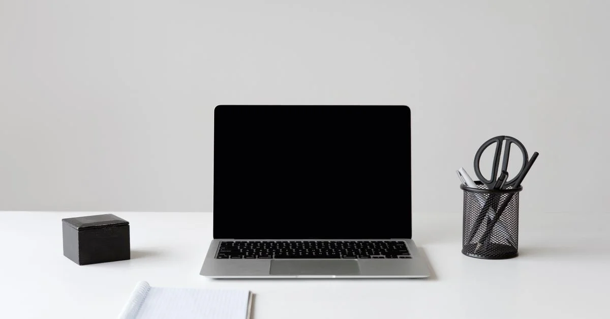 Espace de travail moderne et minimaliste avec un ordinateur portable, un carnet et des fournitures sur une surface blanche.