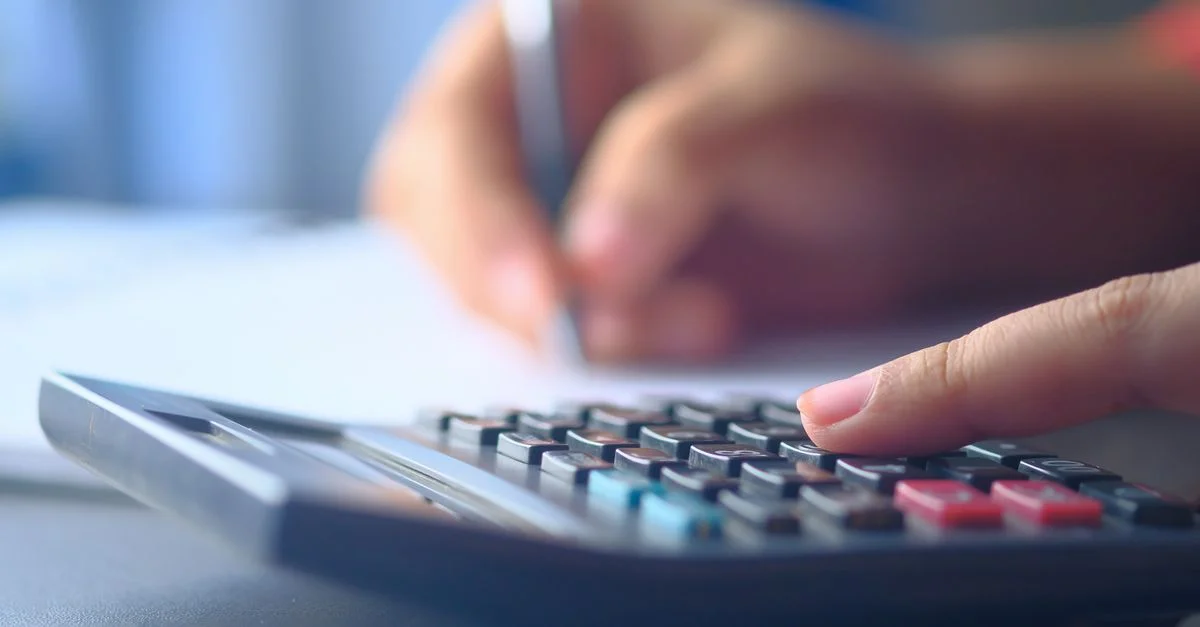 Une image en gros plan de mains utilisant une calculatrice et écrivant, représentant la budgétisation et la planification financière.