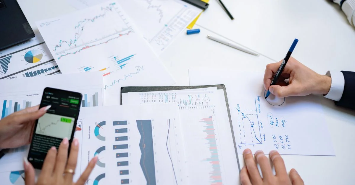 Des collègues collaborant sur des graphiques et des tableaux financiers en utilisant des documents mobiles et sur papier dans le bureau.