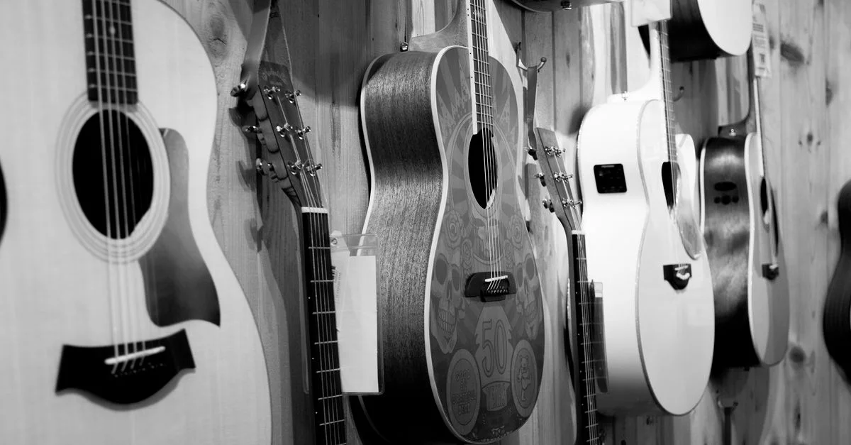Guitares acoustiques montées au mur dans un magasin de musique, photo en noir et blanc.