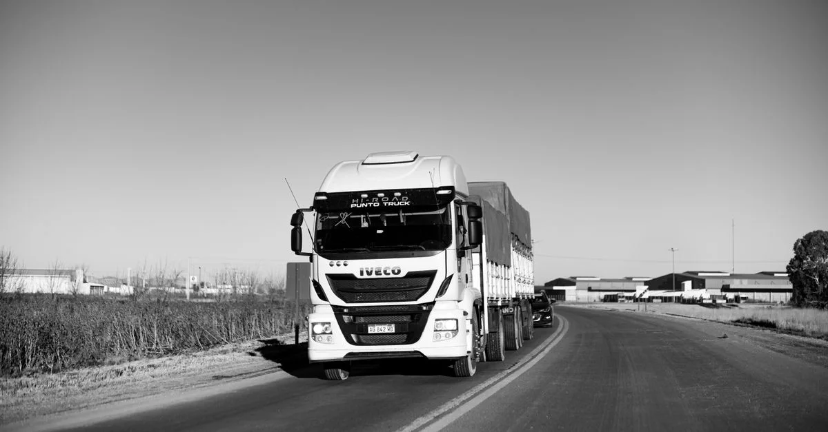 Image monochrome d'un camion roulant sur une autoroute rurale, mettant l'accent sur la vie urbaine.