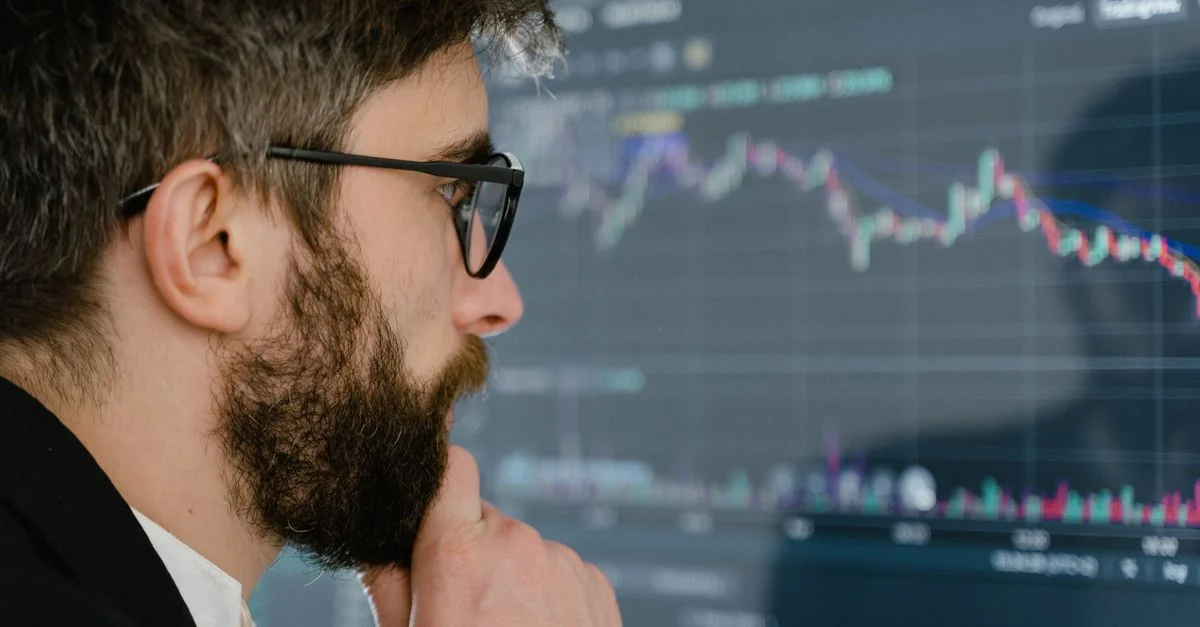 Un homme concentré avec des lunettes étudie des graphiques boursiers sur un écran, réfléchissant à des conclusions.