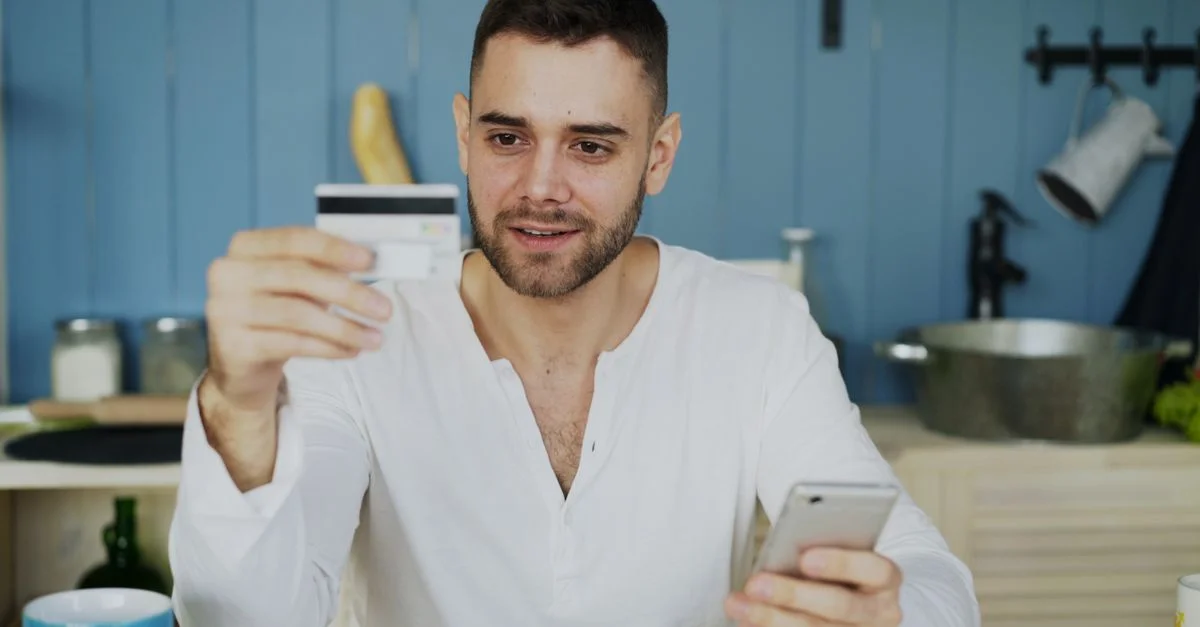 Homme tenant une carte de crédit et un smartphone, faisant des achats en ligne à la maison.