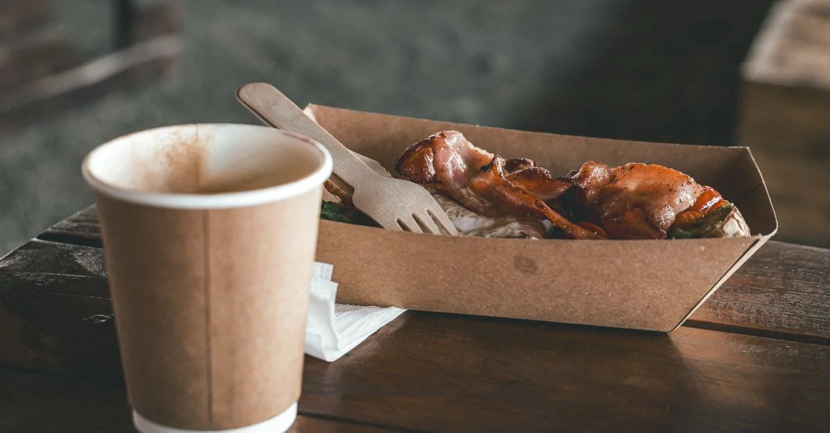 Plats gastronomiques de rue au bacon servis avec du café chaud dans un emballage écologique sur un marché en plein air.