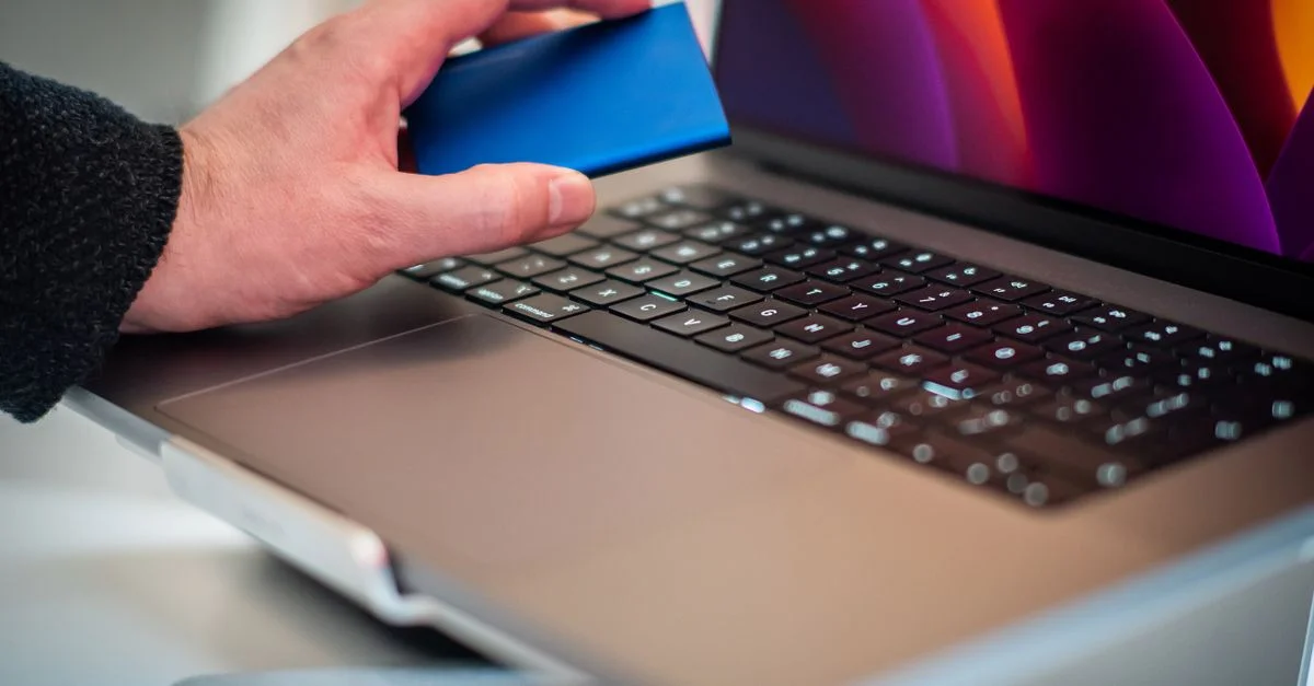 Gros plan d'une main tenant un disque dur externe au-dessus du clavier d'un ordinateur portable.
