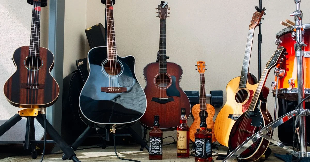 Collection de guitares acoustiques et de bouteilles de Jack Daniels dans un setup musical.
