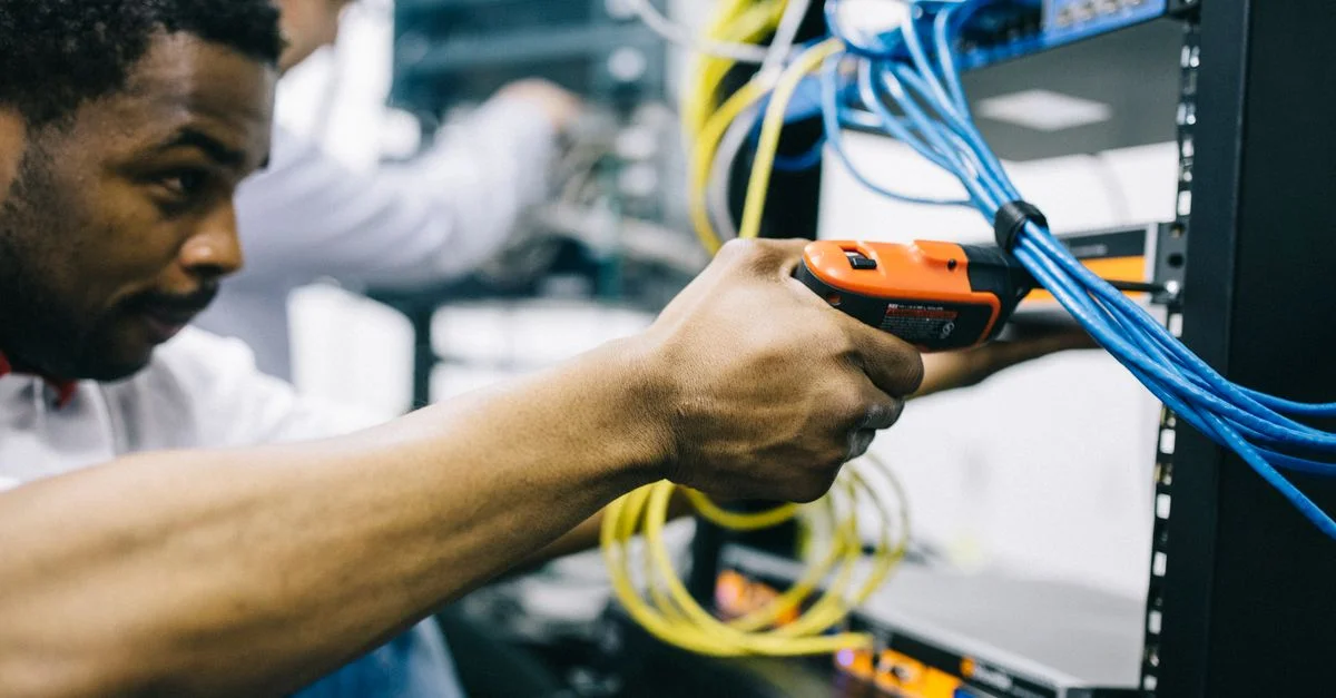 Un ingénieur inspecte des câbles réseau et des connexions dans une salle de serveur, en se concentrant avec précision.