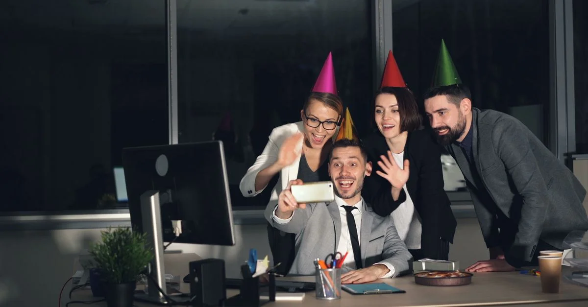 Au bureau, les collègues célèbrent l'événement avec des chapeaux de fête et prennent un selfie joyeux.