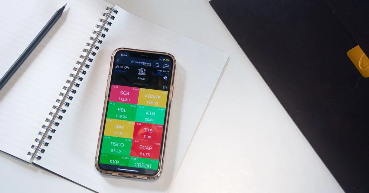 Un smartphone affiche une application financière de marché boursier sur un bureau avec un carnet et un crayon.