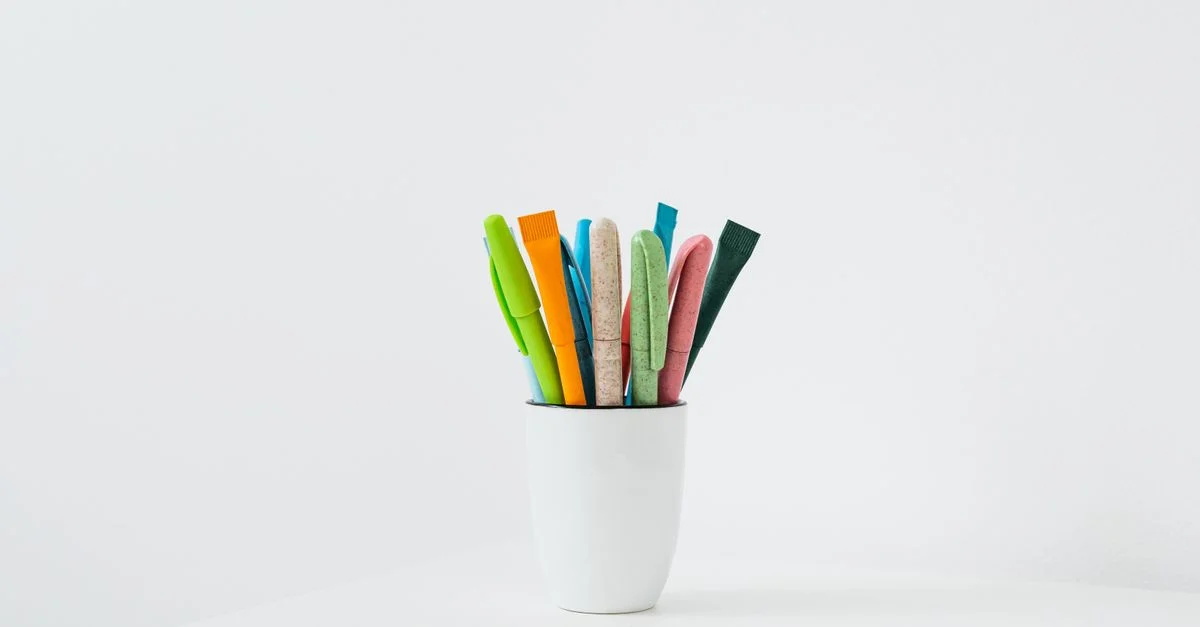 Des stylos colorés disposés dans un porte-stylo en céramique blanche, parfaits pour un bureau ou un espace créatif.