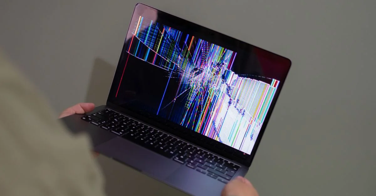 Un écran d'ordinateur portable cassé affichant un glitch coloré tenu par une personne.