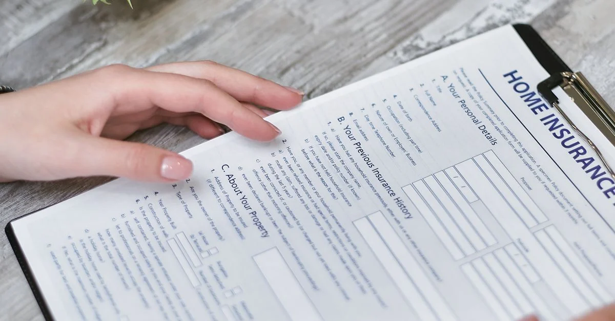 Gros plan sur des mains tenant un document d'assurance habitation à l'intérieur, montrant la section des détails personnels.