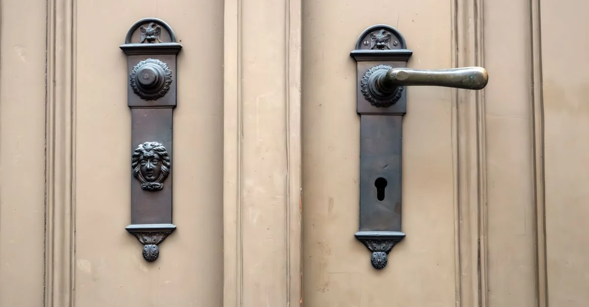 Porte ancienne ornée d'une poignée et d'un bouton de porte en métal finement ouvragés sur une surface en bois.