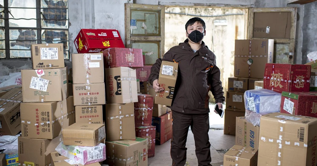 Travailleur de livraison tenant des colis dans un entrepôt à Wuhan, portant un masque facial.