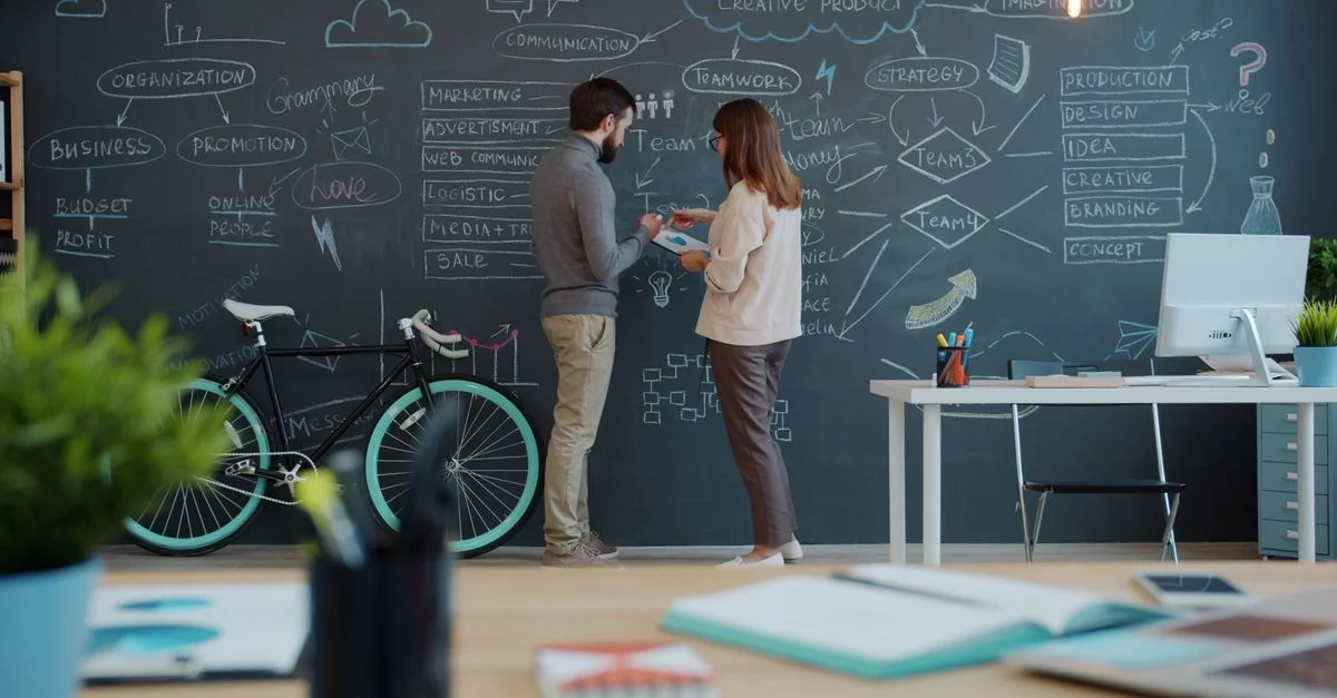 Des membres de l'équipe réfléchissent à des idées novatrices sur un tableau noir dans un espace de bureaux dynamique.