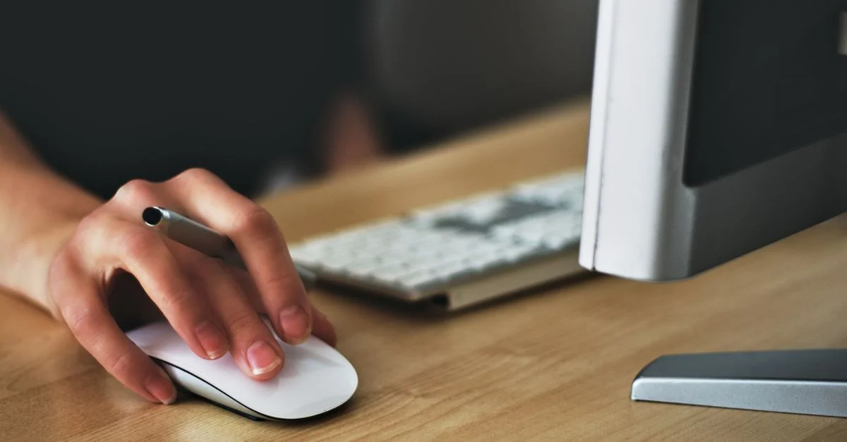 Une main utilisant une souris sans fil sur un bureau moderne avec un ordinateur et un clavier.