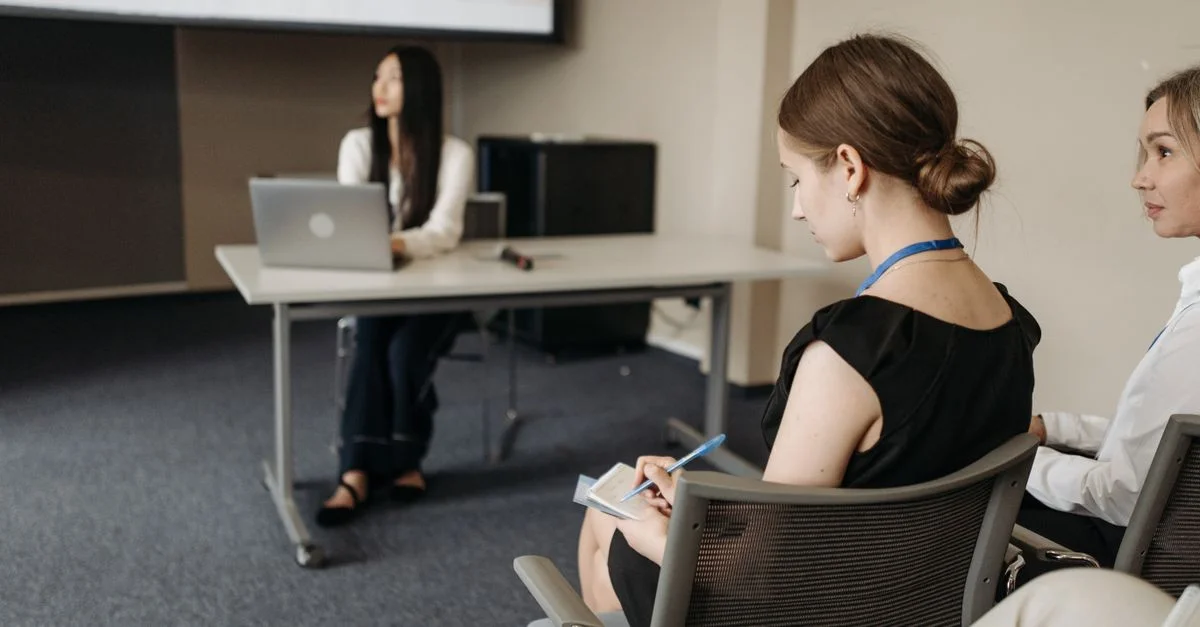 Des participants prennent des notes lors d'une conférence professionnelle en intérieur, concentrés sur la présentation.