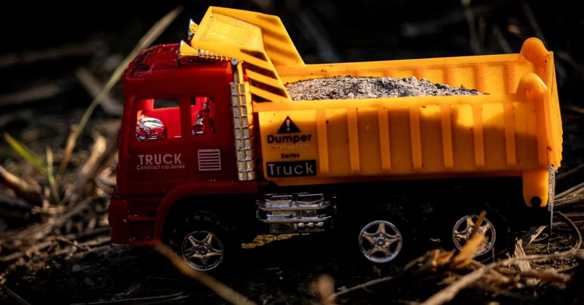 Un camion-benne miniature aux couleurs vives, rempli de gravier, photographié en extérieur à la lumière naturelle.