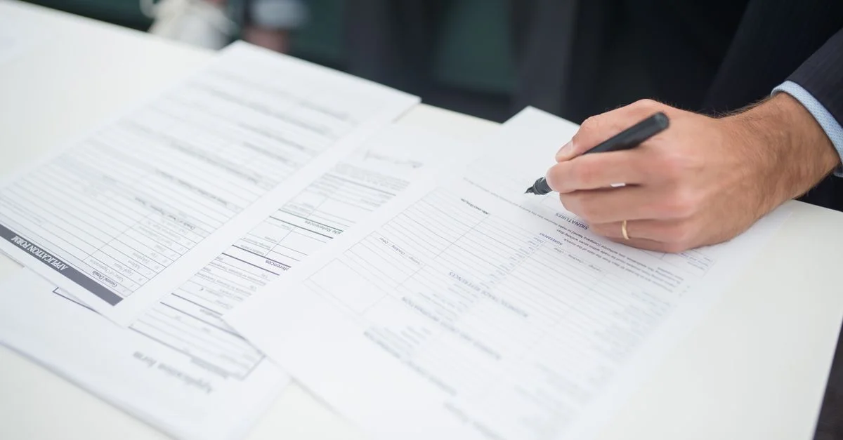 Gros plan d'une main signant des documents d'assurance dans un cadre de bureau.