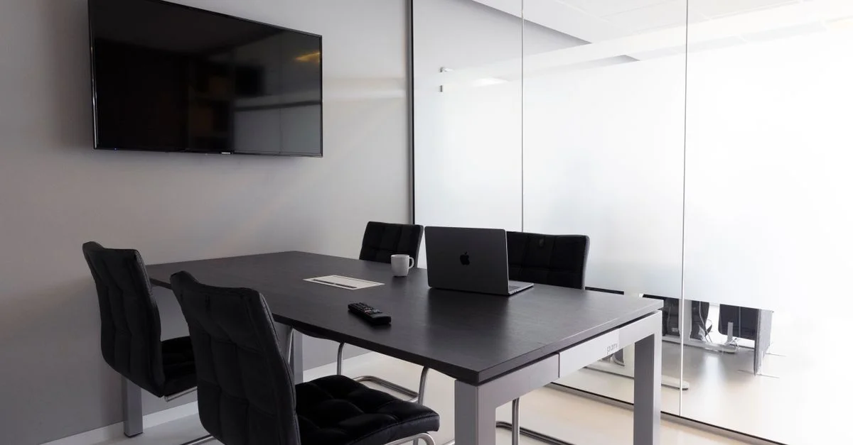 Salle de réunion contemporaine avec des murs en verre, un ordinateur portable et une télévision pour des discussions d'affaires.