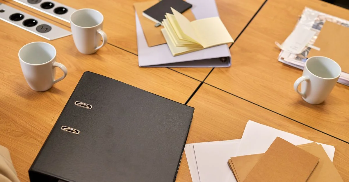 Un bureau de travail bien rangé avec des classeurs, des papiers et des tasses à café disposés de manière ordonnée, offrant une ambiance professionnelle.