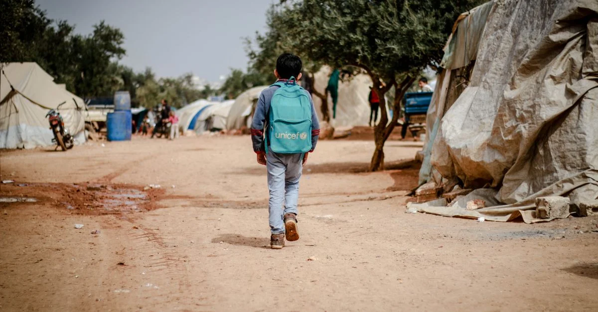 Un jeune garçon marche à travers un camp de réfugiés à Idlib, en Syrie, portant un sac à dos.