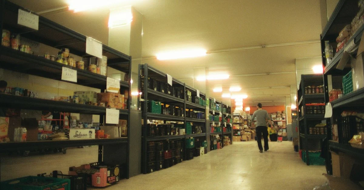 Grand entrepôt à Alfafar, en Espagne, avec des étagères remplies de divers produits et une personne marchant dans l'allée.