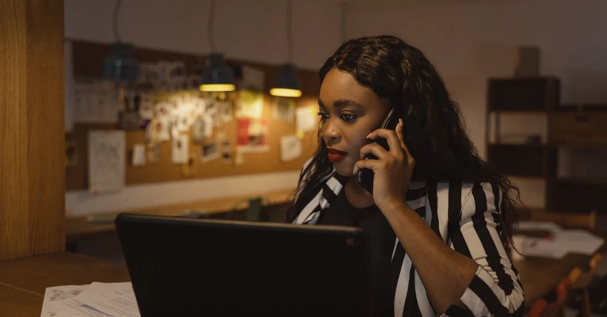 Femme afro-américaine en blazer rayé passant un appel téléphonique dans un bureau moderne.