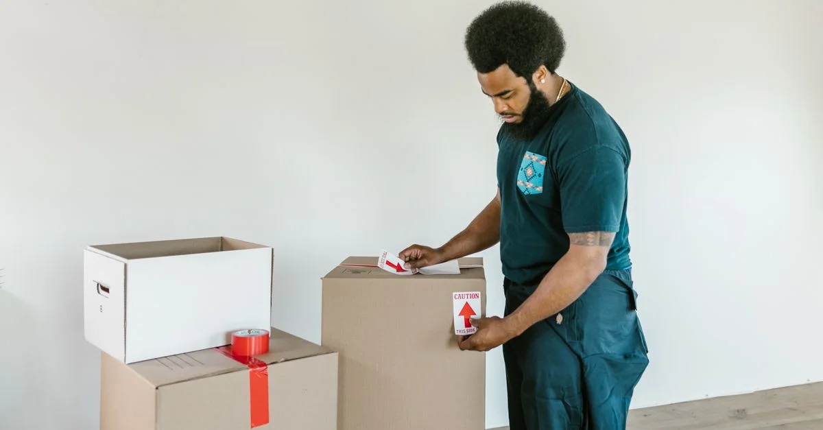 Un homme préparant des cartons de déménagement avec des autocollants de précaution dans un environnement intérieur lumineux.