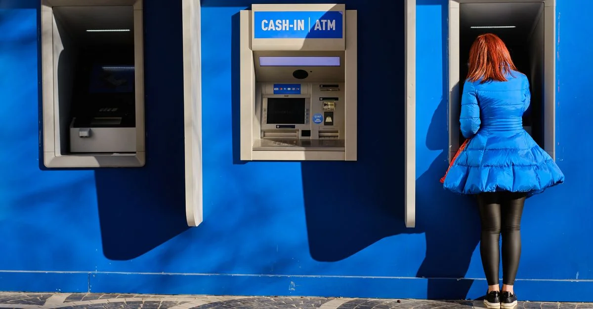 Femme rousse en robe bleue près d'un guichet automatique contre un mur bleu vif à Bakou, Azerbaïdjan.