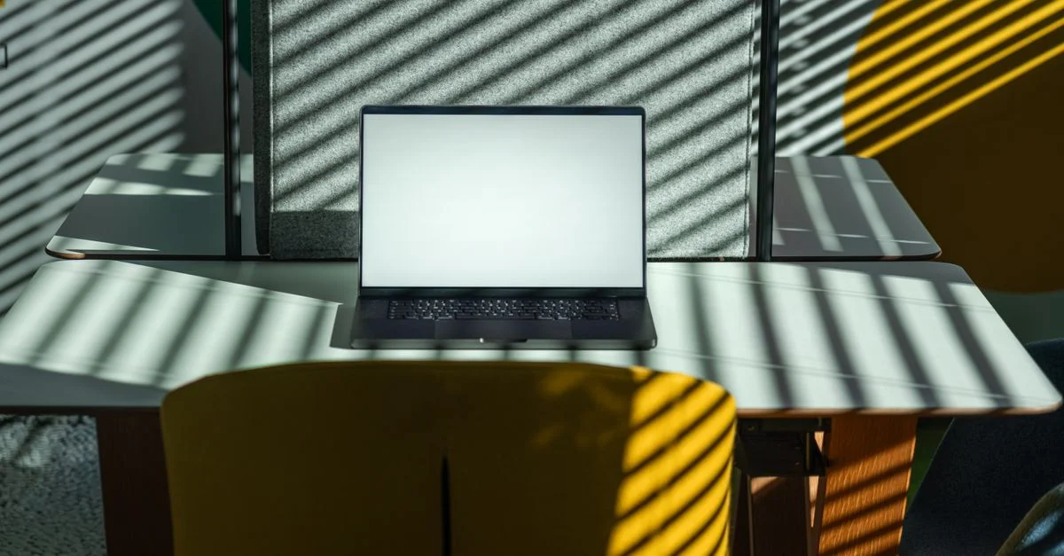 Un espace de bureau moderne avec un ordinateur portable, présentant des ombres géométriques créées par la lumière du soleil à travers des stores.