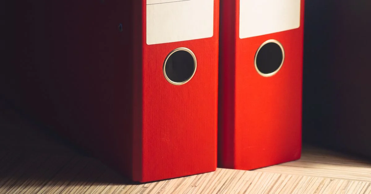 Gros plan sur deux classeurs à levier rouges sur un bureau en bois dans un cadre de bureau moderne.