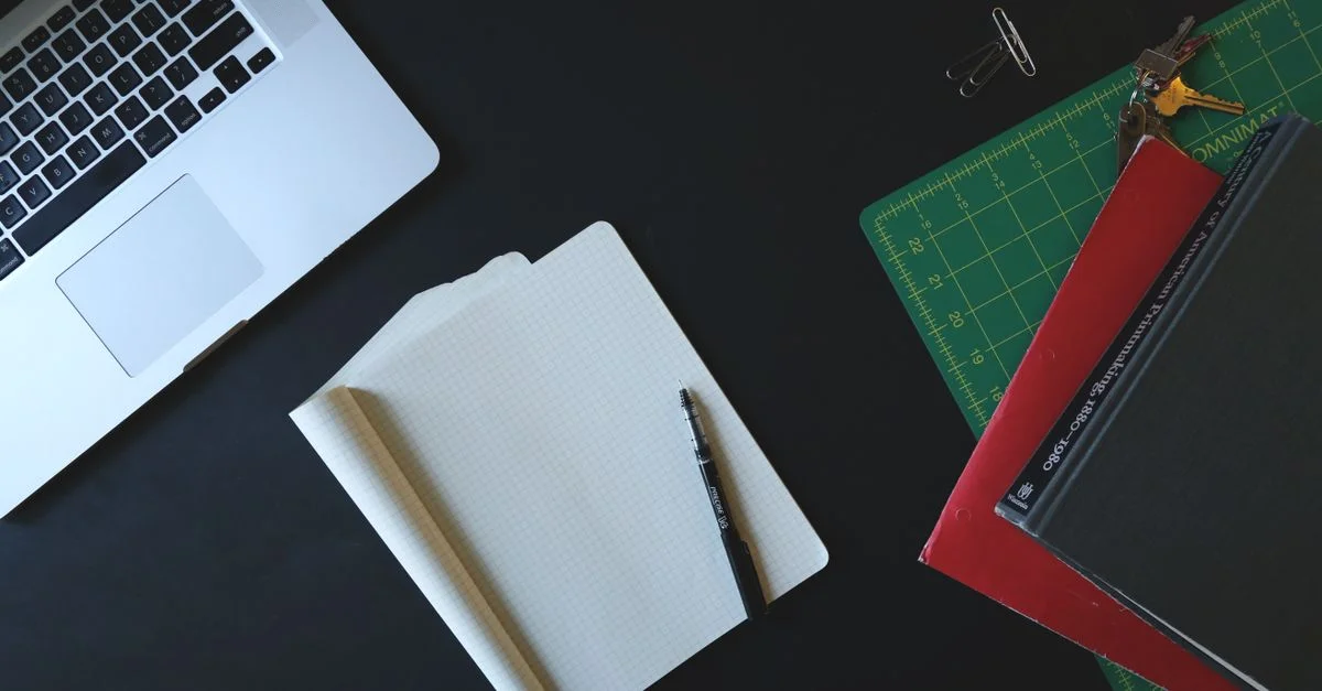 Vue de dessus d'un espace de travail moderne avec un ordinateur portable, un carnet et des fournitures de bureau sur un bureau noir.