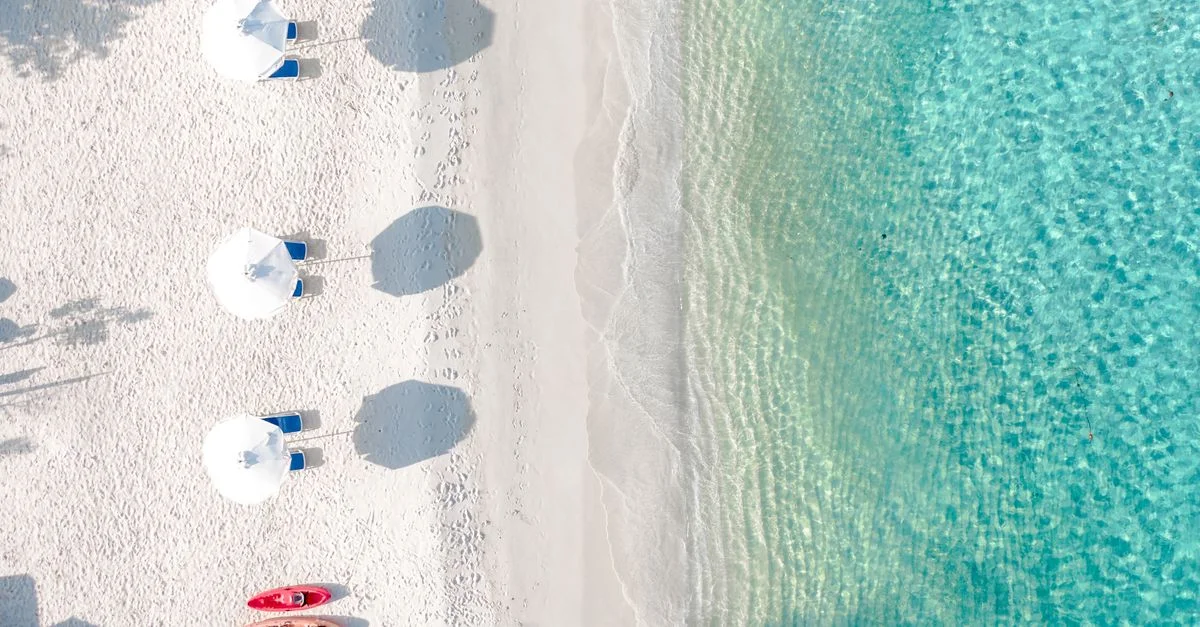 Une prise de vue aérienne sereine d'une plage immaculée avec du sable blanc, des parasols et une eau turquoise.