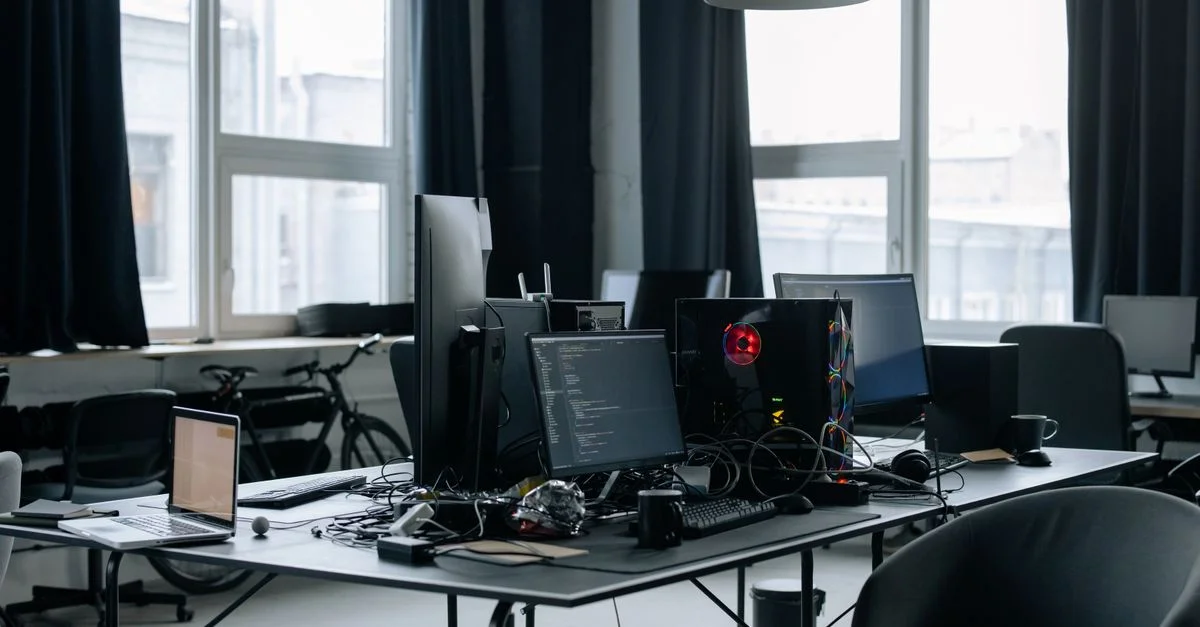 Espace de travail contemporain avec des ordinateurs, des écrans de codage et des essentiels de bureau dans un environnement technologique.