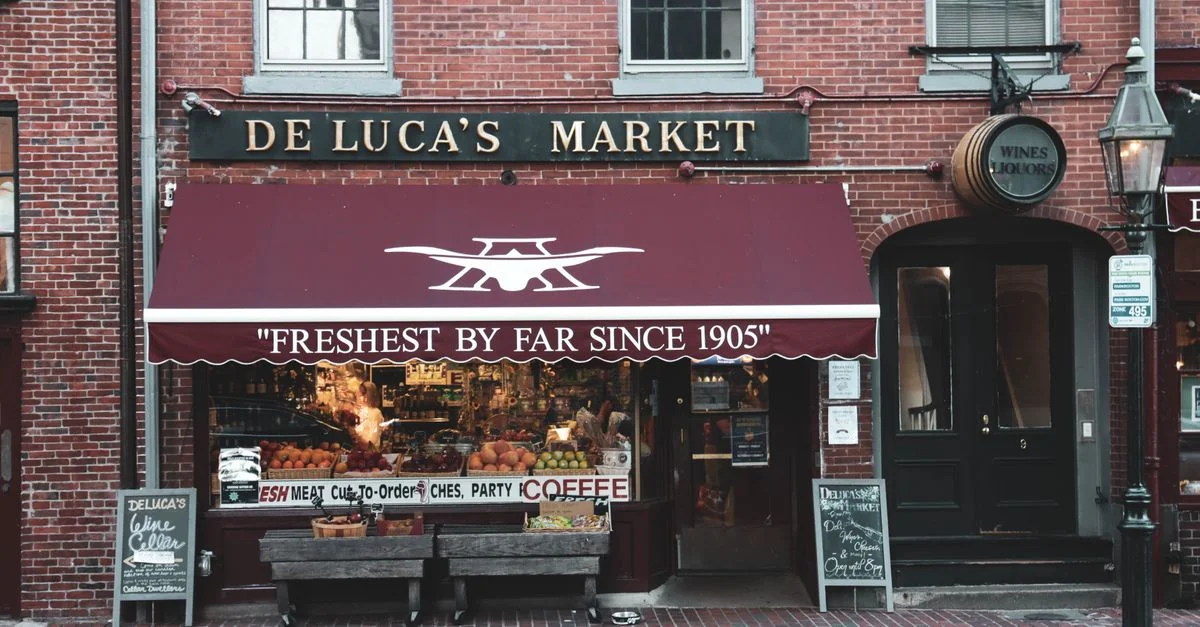 Façade historique du marché De Luca montrant des produits frais et une atmosphère urbaine conviviale.