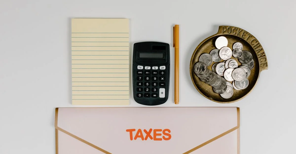 Un plan à plat des essentiels pour la préparation des impôts : calculatrice, pièces, bloc-notes, stylo et dossier.