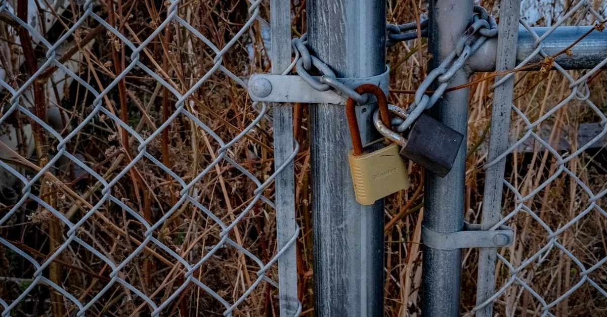 Un gros plan d'une clôture en mailles avec des cadenas la sécurisant, symbolisant une haute sécurité à l'extérieur.