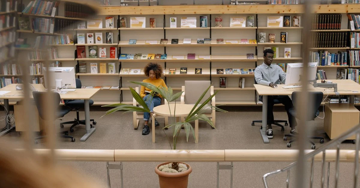 Scène de bibliothèque intérieure avec des étudiants divers étudiant à des bureaux entourés d'étagères de livres.