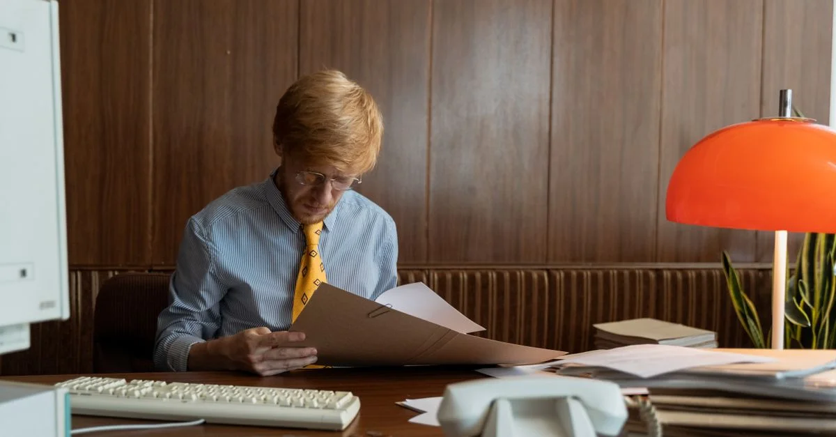 Homme dans un bureau rétro révisant des documents sous une lumière chaleureuse. Idéal pour des thèmes d'affaires.