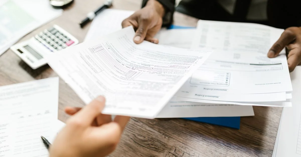 Deux professionnels échangent des documents dans un cadre de bureau, mettant l'accent sur la paperasse et l'analyse de données.
