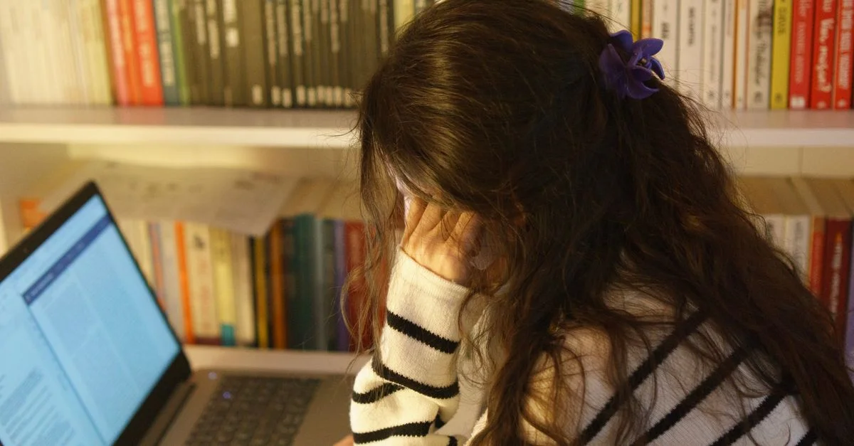Une femme dans une bibliothèque utilisant un ordinateur portable, semblant stressée en étudiant. Parfait pour des thèmes éducatifs ou de santé mentale.