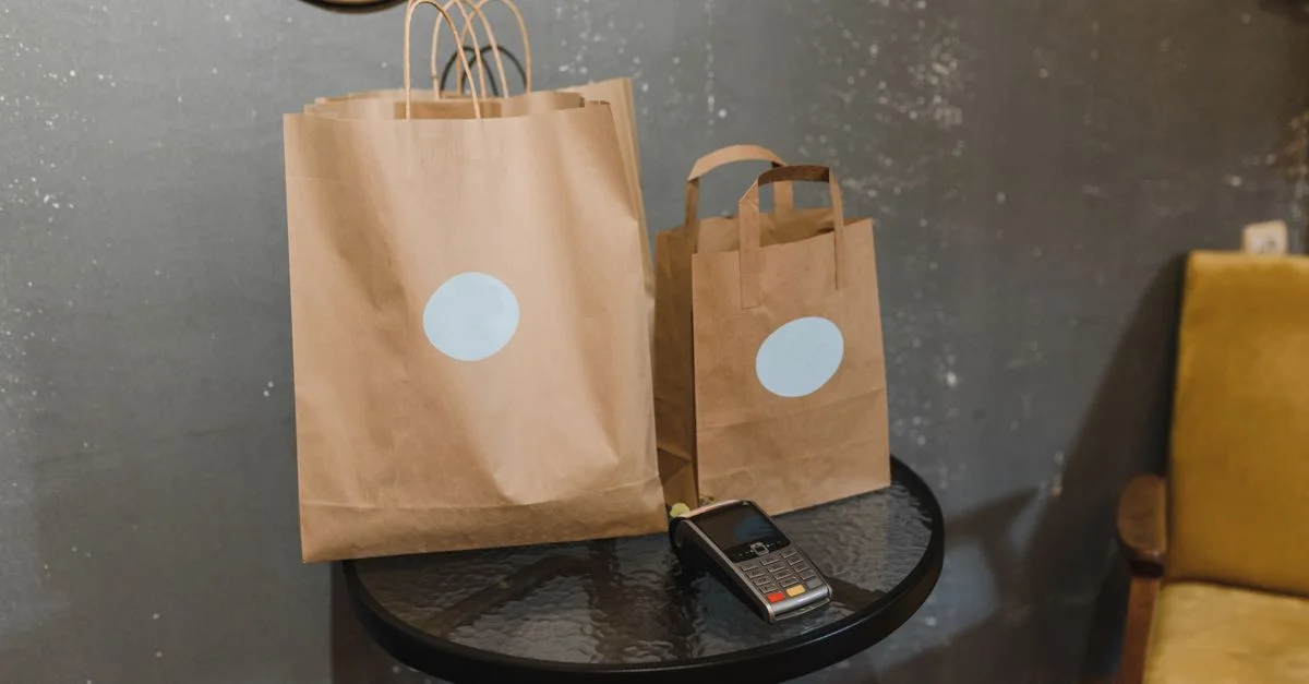 Des sacs en papier marron sur une table à côté d'un terminal de paiement dans une pièce confortable.