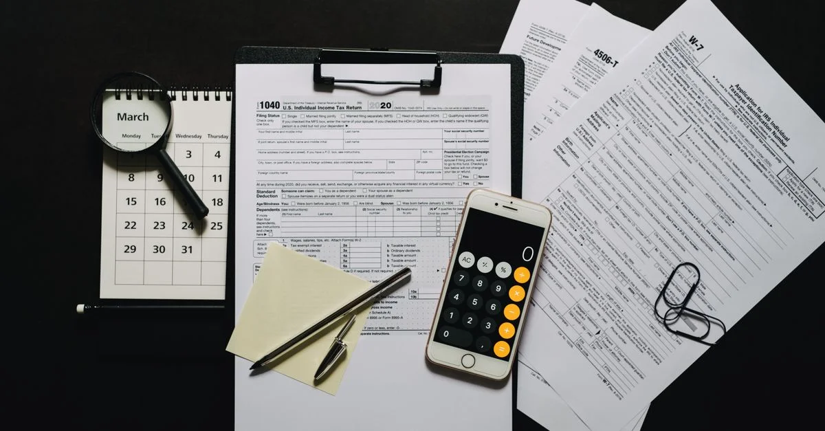 Vue du dessus des documents fiscaux, d'une calculatrice, d'une loupe, et d'un calendrier sur une surface noire.