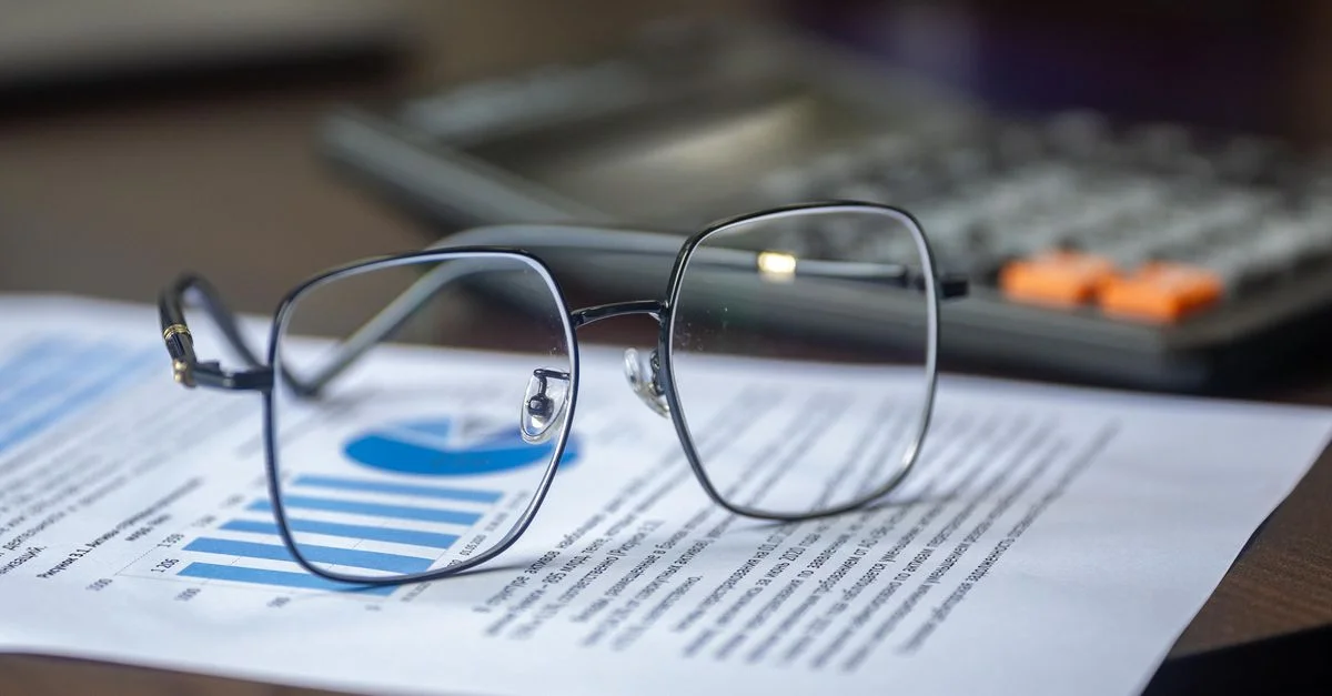 Lunettes sur un rapport financier avec une calculatrice dans un bureau, mettant en avant l'analyse.