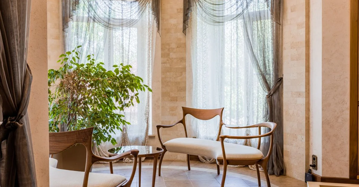 Espace de détente élégant avec des chaises en bois et des rideaux fluides dans une pièce lumineuse.