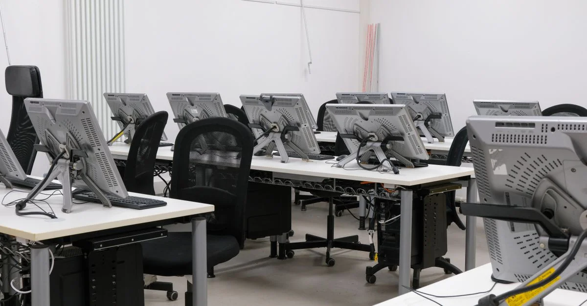 Une salle informatique vide, équipée de plusieurs postes de travail avec écrans et chaises, prêts à l'emploi.