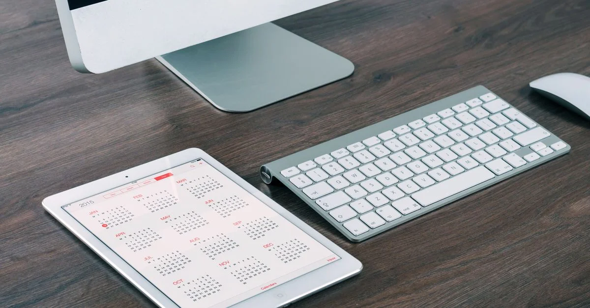 Un espace de travail élégant et moderne avec un iMac, un iPad avec calendrier, un clavier et une souris.