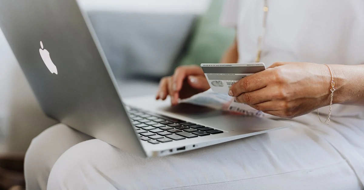 Gros plan sur une personne tenant une carte de crédit tout en faisant des achats en ligne avec un ordinateur portable à la maison.